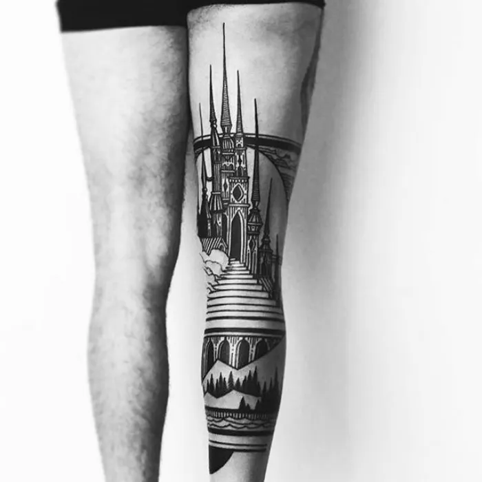 Leg with intricate architecture tattoo featuring a gothic-style castle and bridge in black ink.