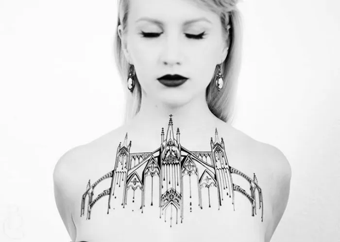 Monochrome image of a woman with a detailed architecture tattoo across her chest.