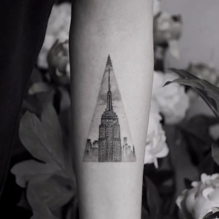 Architecture tattoo of a skyscraper framed in a triangular design on an arm.