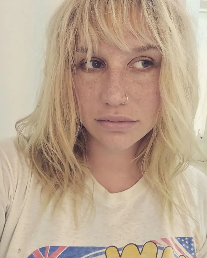 Celebrity with tousled blonde hair and a nose ring, wearing a graphic t-shirt, showcasing a natural look without makeup.