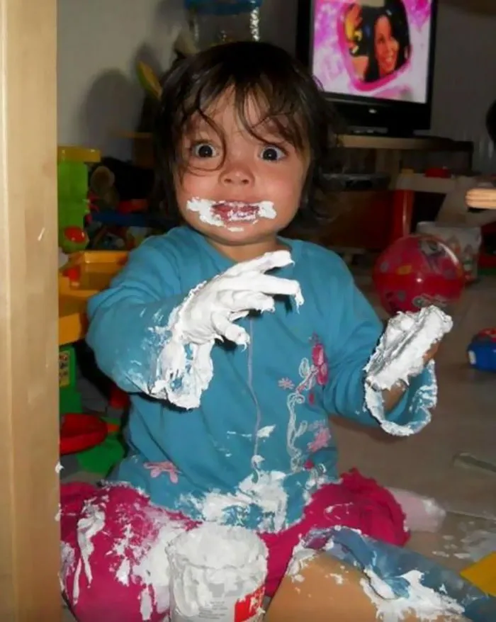 Child covered in cream, wide-eyed with surprise, showcasing a hilarious moment when left alone.