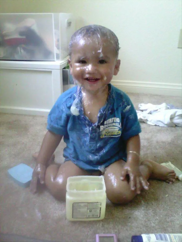 Child covered in cream, smiling on the carpet, highlighting the hilarious results of leaving kids alone.