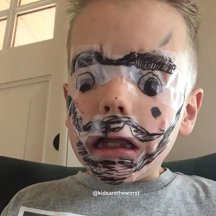 Child with face covered in taped drawings showing hilarious creativity when left alone.