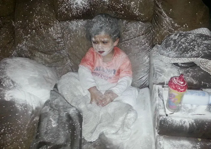 Child covered in white powder after being left alone on a couch, illustrating a humorous parenting moment.
