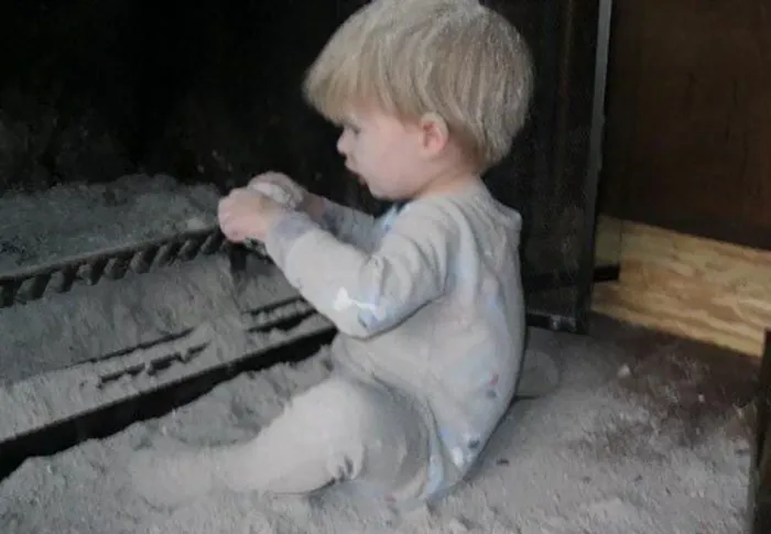 A toddler plays in a fireplace filled with ash, illustrating what happens when kids are left alone.