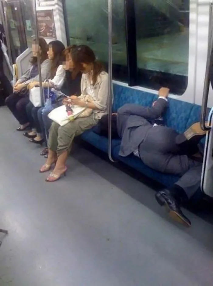 Weirdest subway sighting: person in a suit lying across seats, others seated nearby.