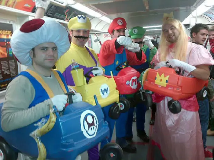 People in colorful costumes holding toy race cars on the subway.