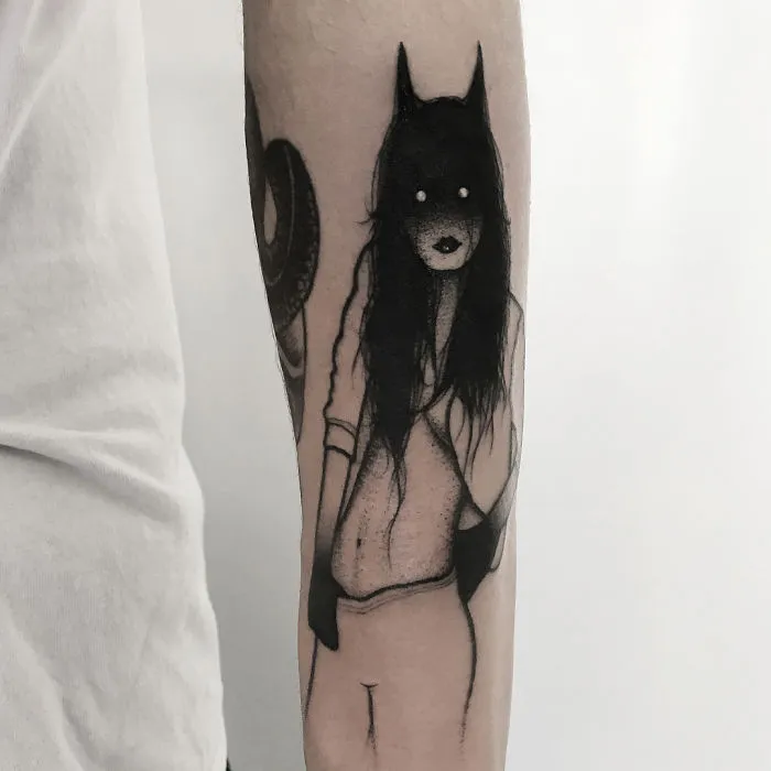 Faceless girl tattoo with dark hair and eerie expression on forearm, featuring a mysterious, slightly erotic design.