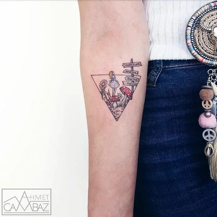 Striking tattoo by Turkish cartoonist featuring Alice in Wonderland and directional sign on a person's forearm.