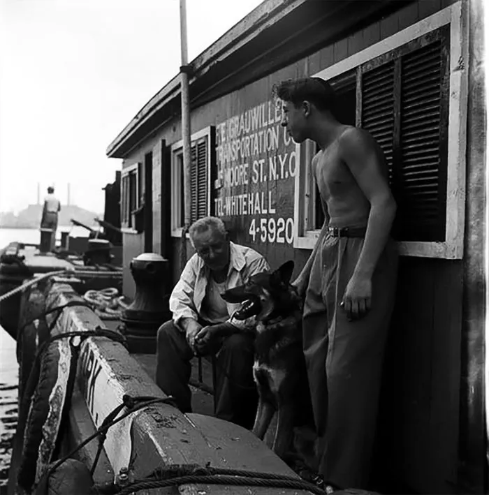 Black and white photo of two men and a dog on a New York dock, taken by 17-year-old Stanley Kubrick in the 1940s.