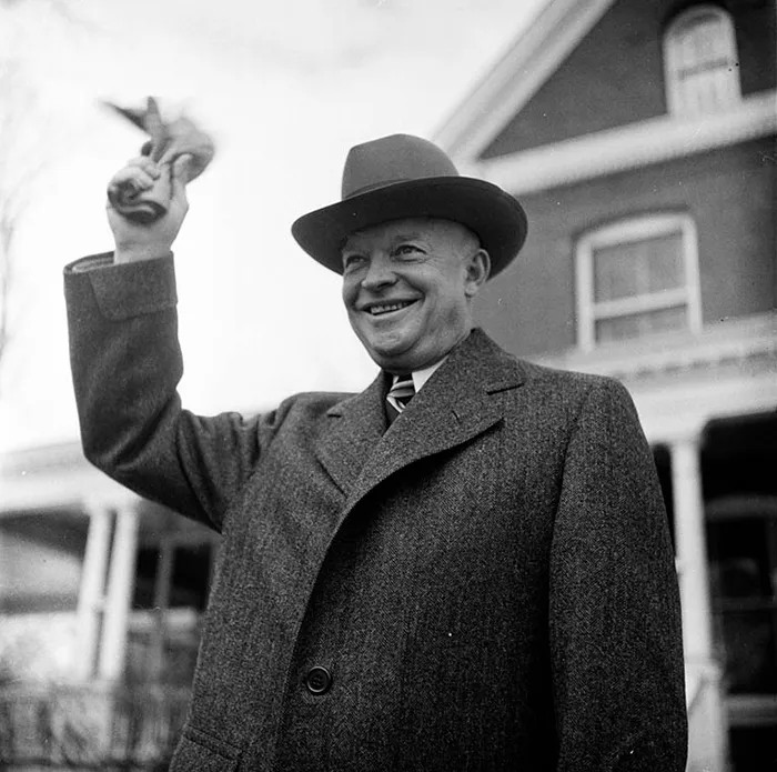 A man in a suit and hat smiling, holding a newspaper, captured by Stanley Kubrick in 1940s New York.