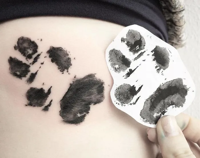 Dog paw print tattoo on skin with matching ink print on paper, showcasing paw print tattoo art.