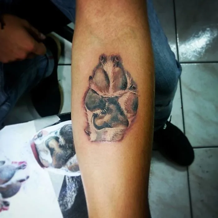 Tattoo of a realistic dog paw print on a person's forearm, showcasing detailed shading and texture.