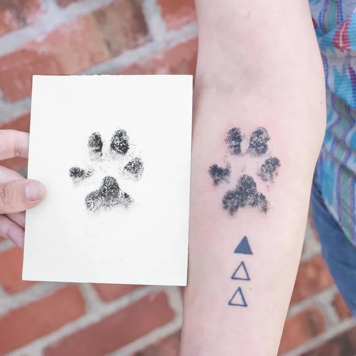Dog paw print tattoo on arm next to an inked paw print on paper, representing unique body art designs.
