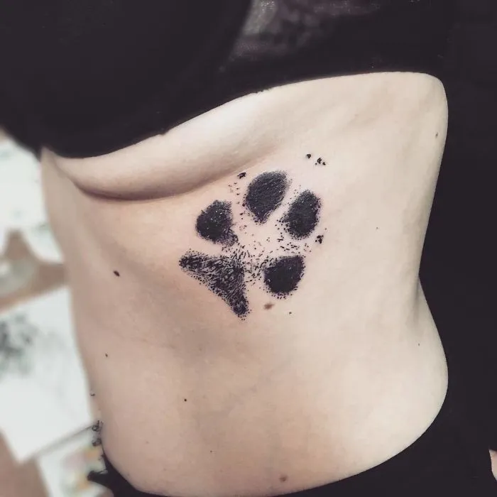 Dog paw print tattoo on a person's side, showcasing detailed and artistic ink work.