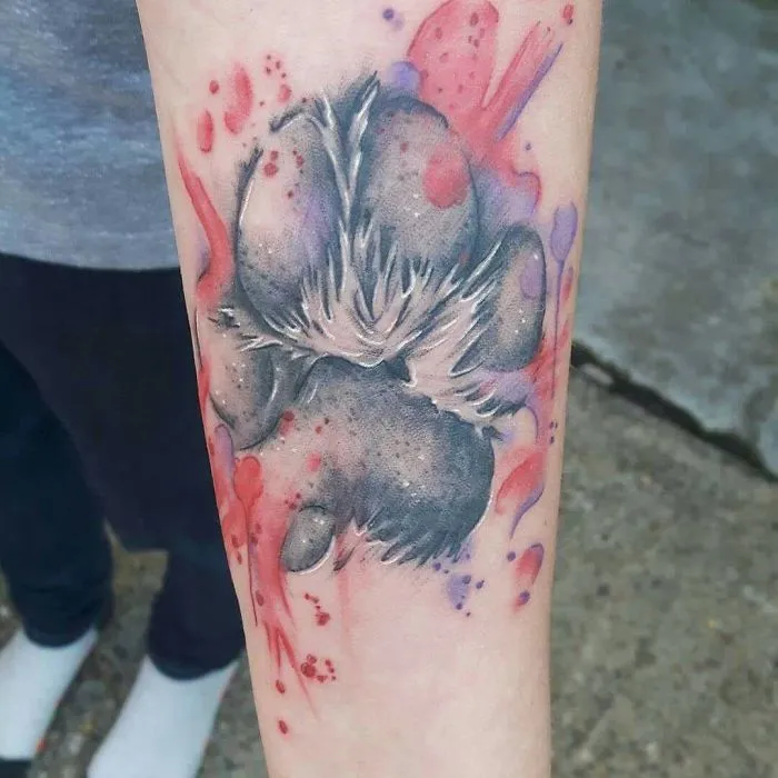 Colorful dog paw print tattoo on forearm, featuring red and purple splashes.