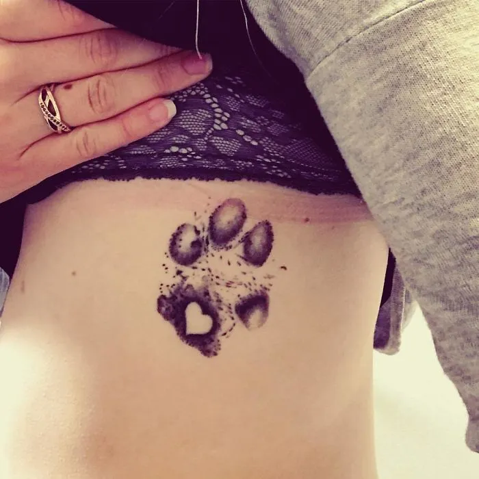 Dog paw print tattoo on skin, featuring a small heart design.