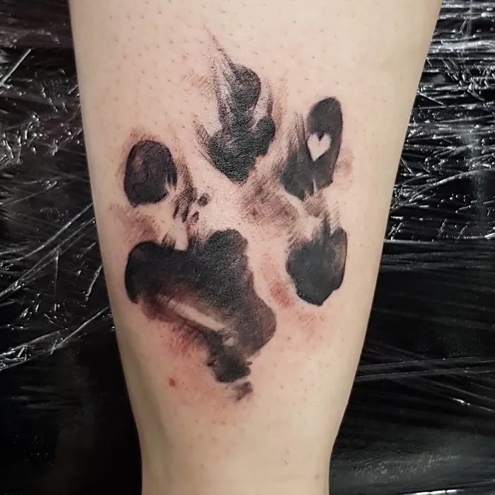 A black ink dog paw print tattoo on a person's arm, showcasing a heart shape in one pad.