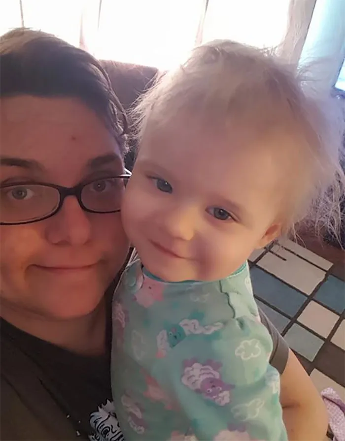 Person with glasses holding a smiling baby, highlighting that depression symptoms have no face.