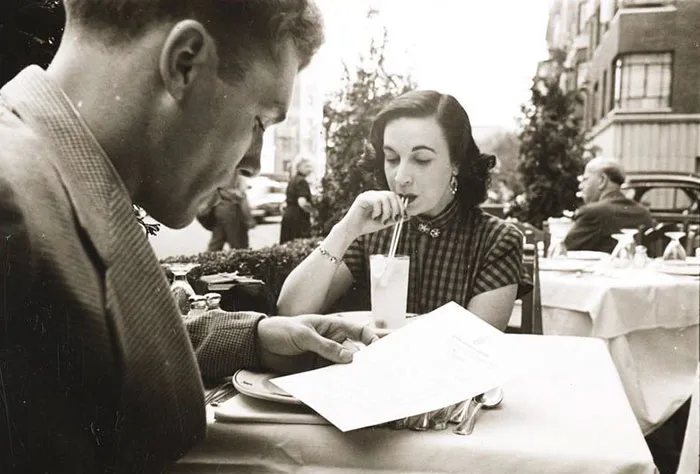 A 1940s New York cafe scene captured by Stanley Kubrick, with a woman sipping a drink and a man reading a menu.