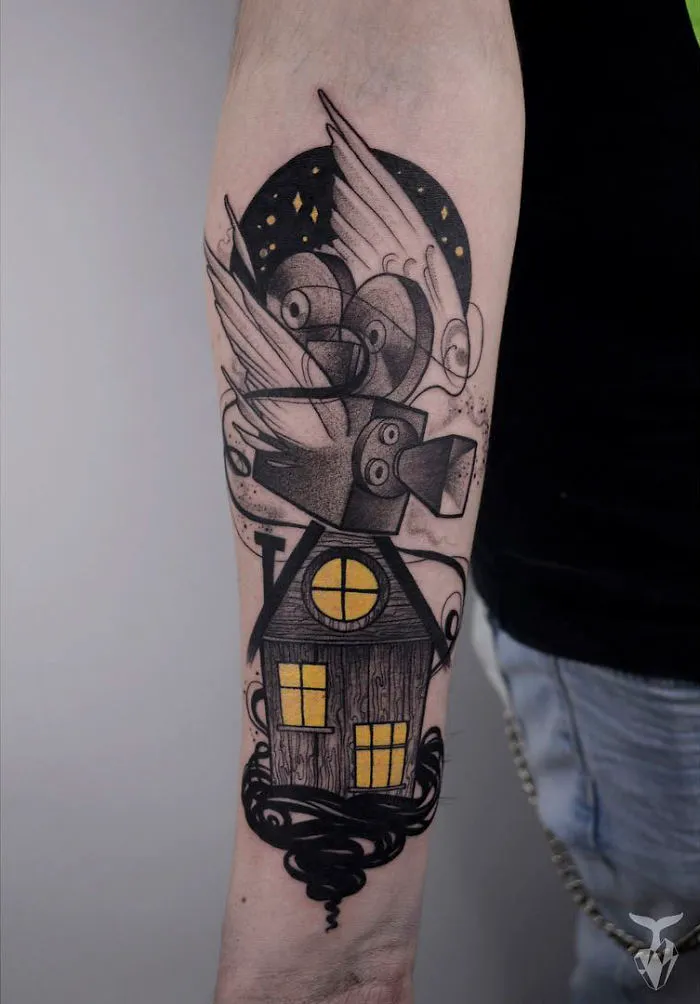 Nature and Art Nouveau inspired tattoo of a house with yellow windows and swirling designs on an arm.