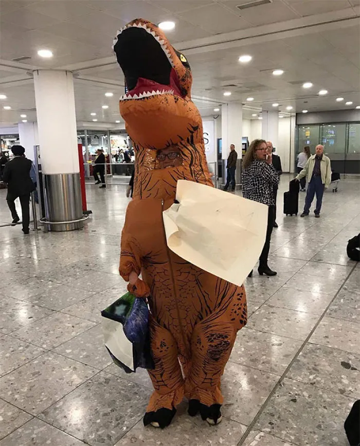Funny airport pickup with person in dinosaur costume holding signs, amusing travelers.