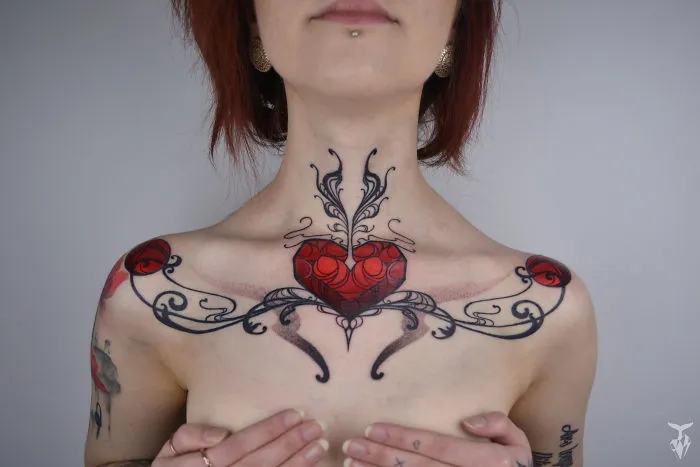 Nature and Art Nouveau inspired tattoo featuring a red heart and intricate black swirls on a woman's chest.