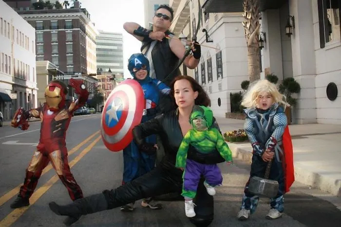 A family dressed in superhero Halloween costumes posing together in the street