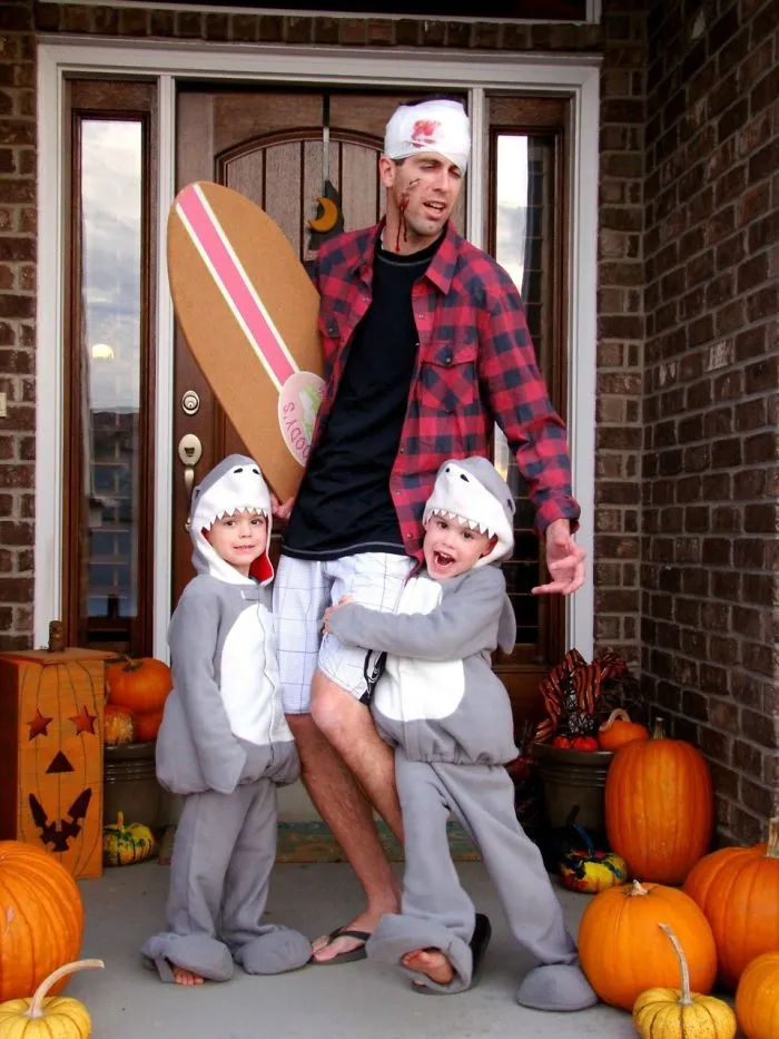 A father and sons in funny shark attack family Halloween costumes on their front porch.