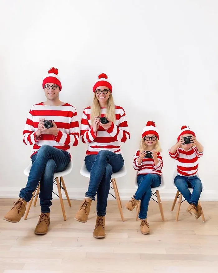A family sitting on white chairs wearing matching Waldo Halloween costumes with cameras