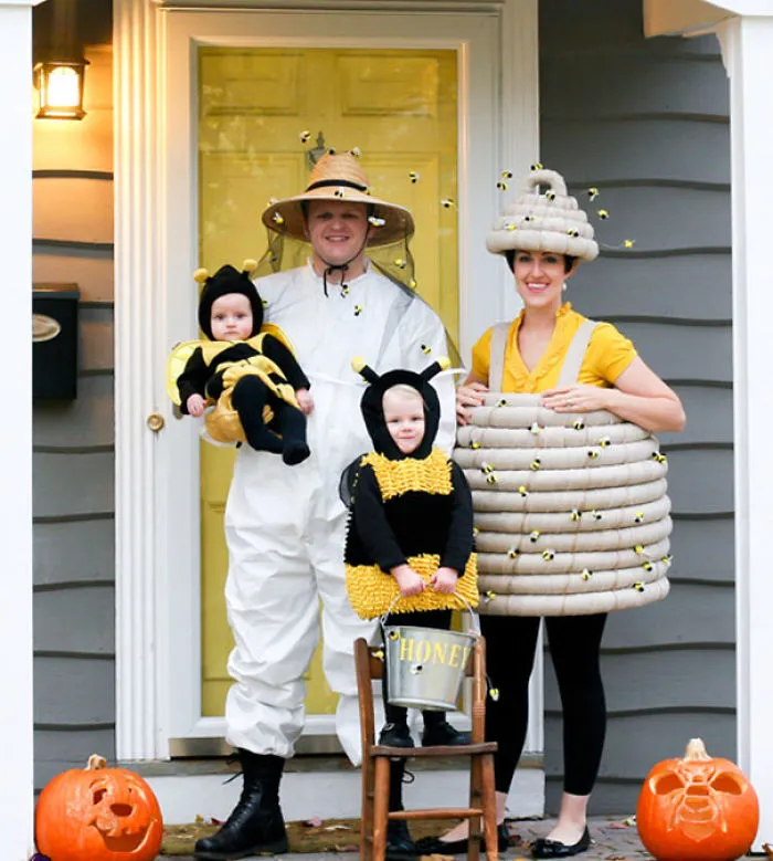 A family dressed as a beekeeper, a beehive, and two small bees posing for Halloween costumes.