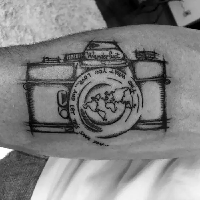 Camera travel tattoo with map design and "Wanderlust" text on a person's arm.