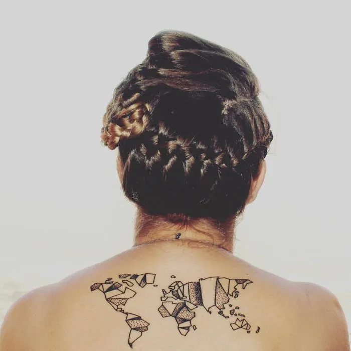 Back view of a person with a world map travel tattoo on their upper back, hair styled in an intricate updo.