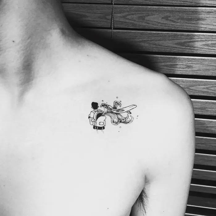 Minimalist travel tattoo of explorer with luggage and airplane on shoulder.