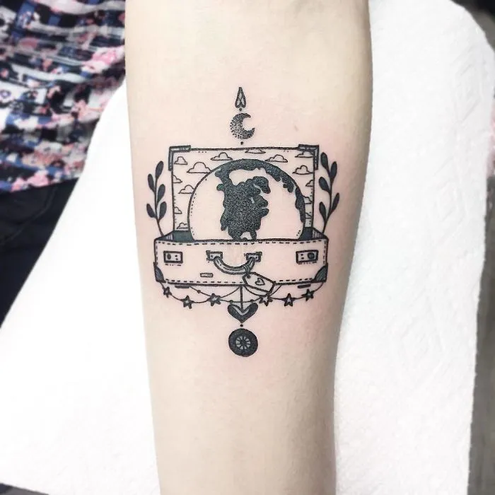 Travel tattoo featuring a suitcase with a globe inside, decorated with stars and plants.