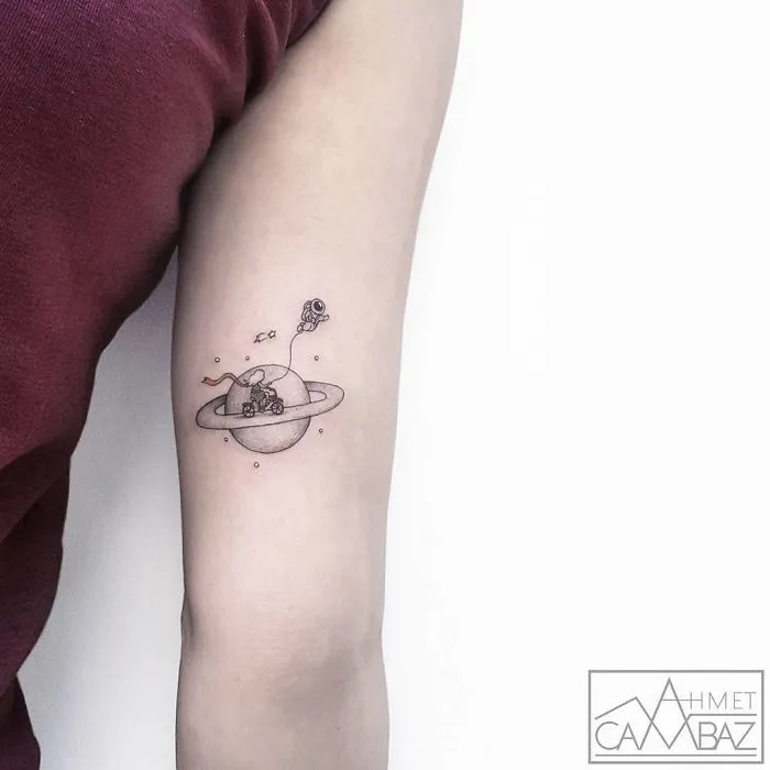 Travel-themed tattoo of a planet with a tiny astronaut, capturing the wanderlust spirit, inked on an arm.