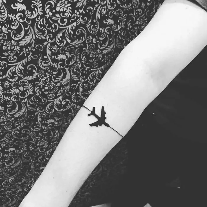 Minimalist travel tattoo of an airplane on a person's forearm, symbolizing adventure and wanderlust.