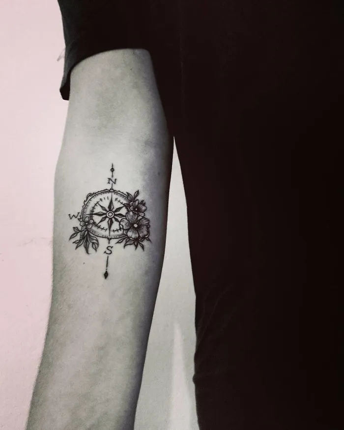 Arm with a travel tattoo featuring a compass and flowers, symbolizing adventure and exploration.