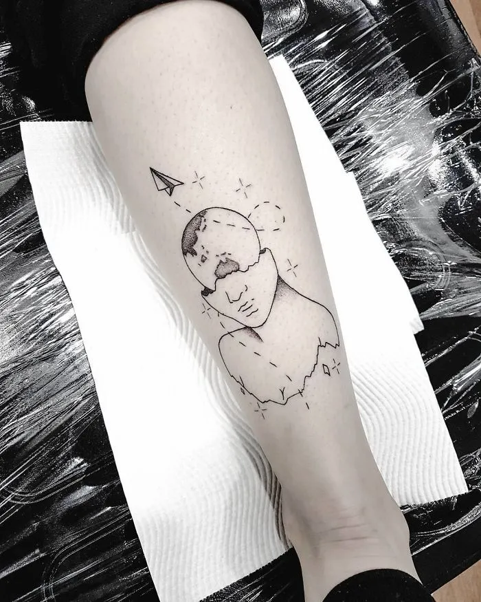 Travel tattoo of a fragmented face with a paper airplane on the leg, symbolizing wanderlust and adventure.