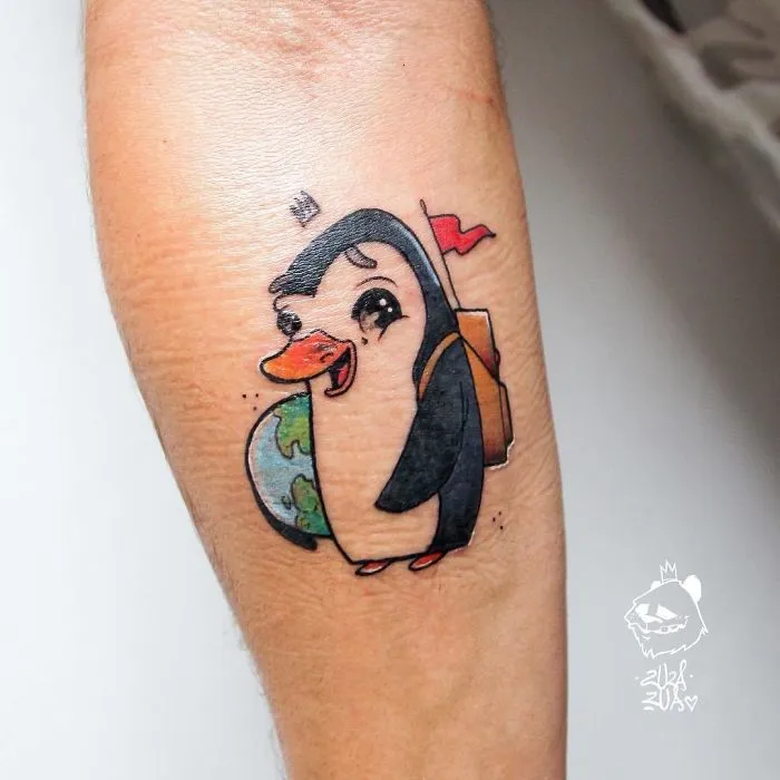 Cartoon penguin travel tattoo with a backpack and globe on arm.