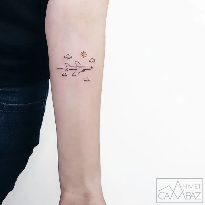 Arm with a small travel tattoo of an airplane surrounded by clouds and a sun, symbolizing travel inspiration.