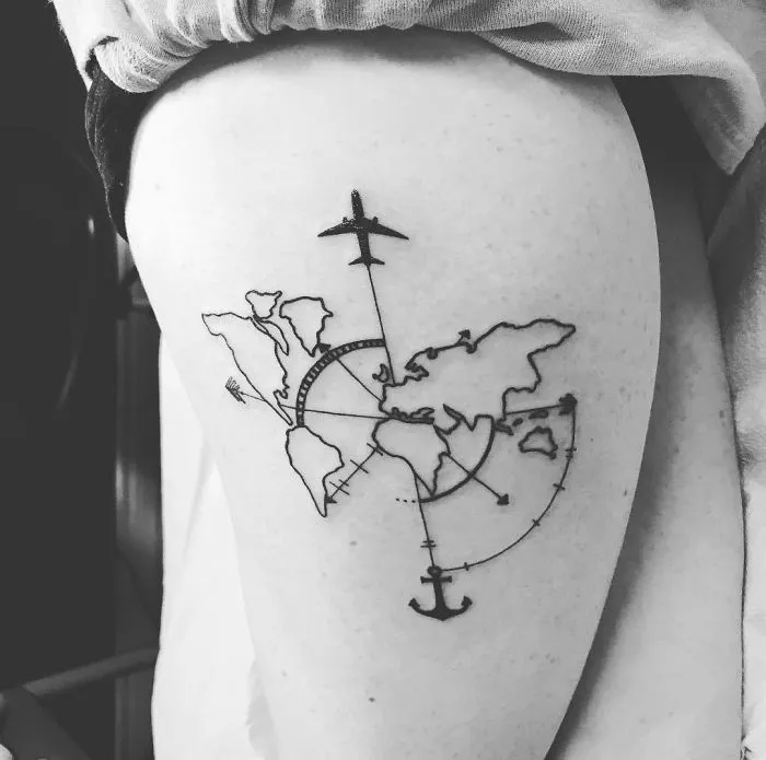 Travel tattoo of a world map, airplane, and anchor on the upper arm in black ink.