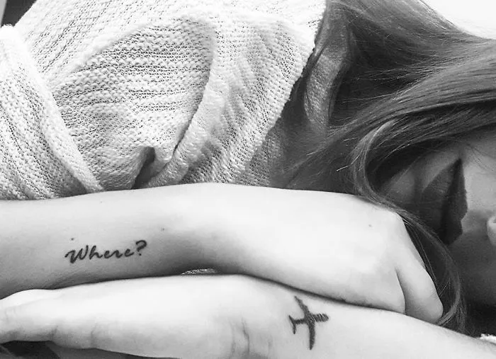 Close-up of travel tattoos on a person's arm, featuring an airplane and the word "Where?"