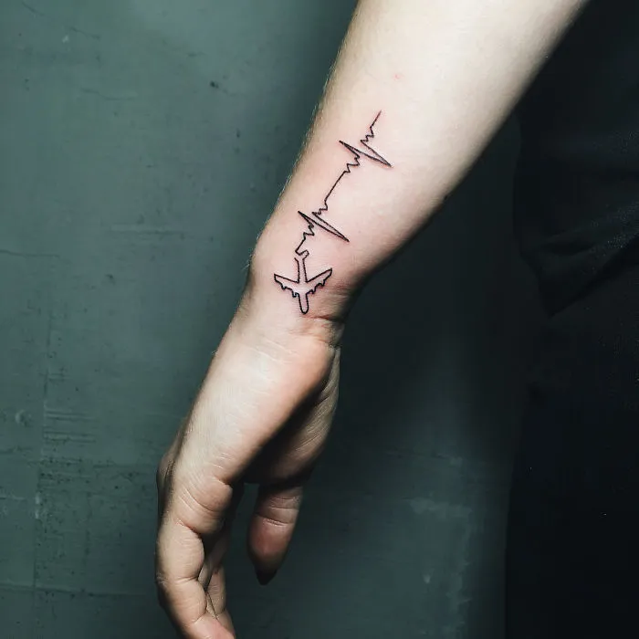 Minimalist travel tattoo of an airplane and heartbeat line on forearm.