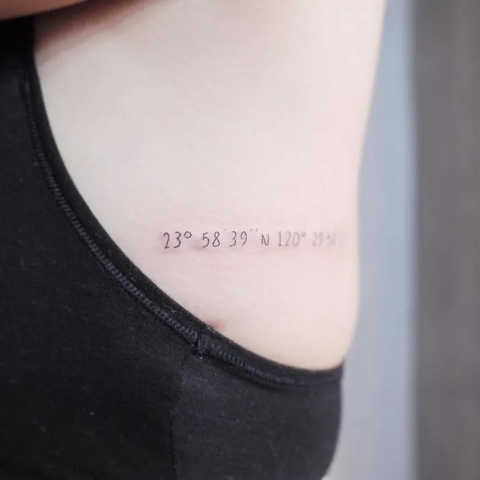 Minimalist travel tattoo with coordinates on the side of the body, suggesting wanderlust and adventure.