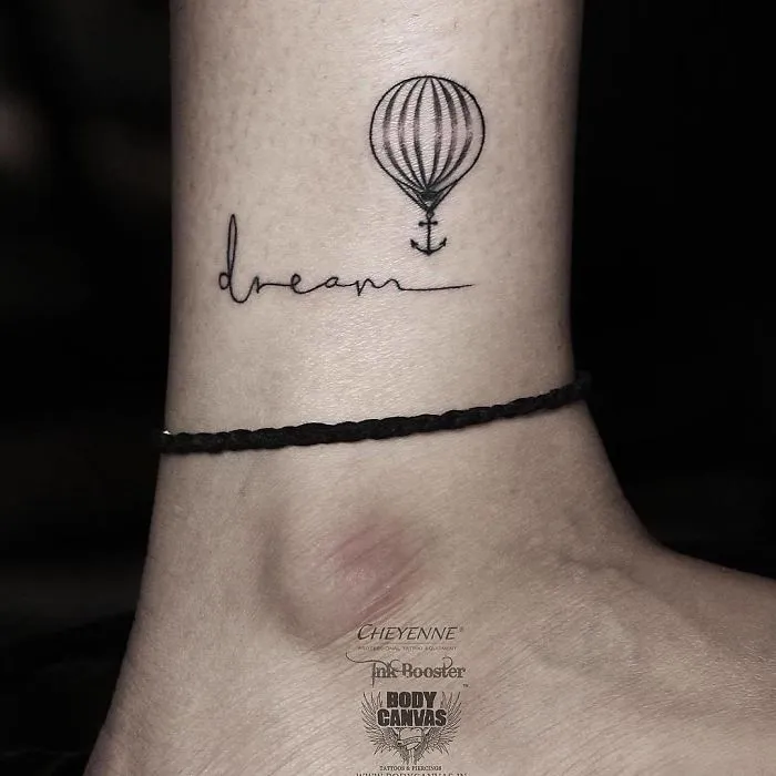 Tattoo of a balloon with "dream" script, symbolizing travel inspiration on someone's wrist.