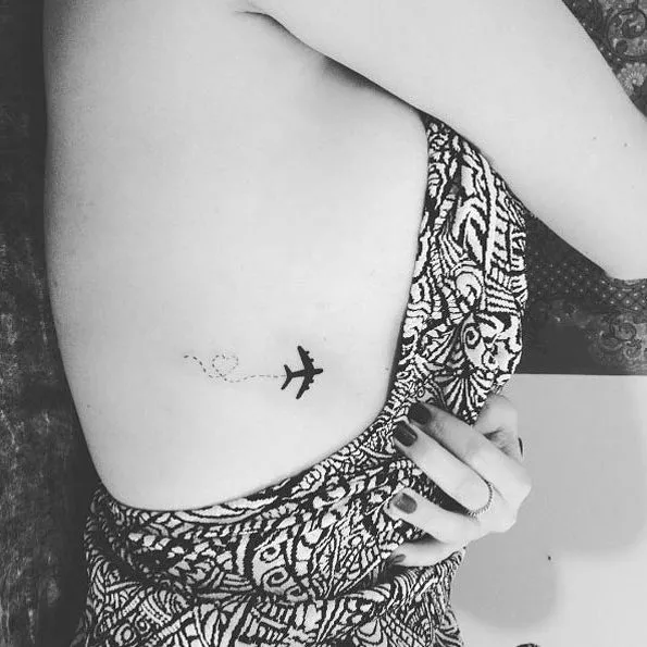 Travel tattoo of a plane on a woman's side, with dotted lines forming a heart, inspiring wanderlust.