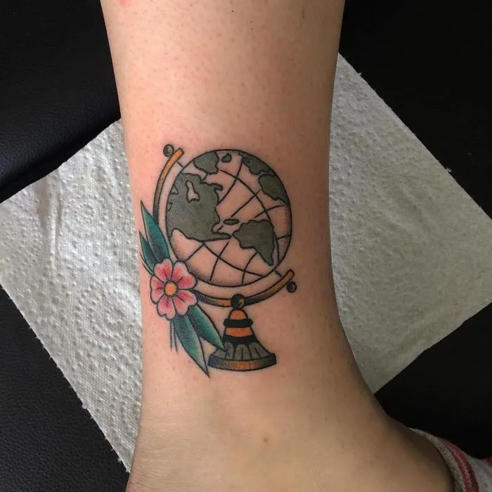 Travel tattoo featuring a globe and a flower on an ankle, symbolizing adventure and wanderlust.
