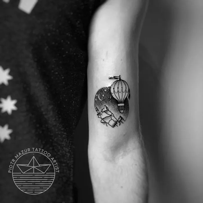 Travel-themed tattoo with a hot air balloon and mountains on an arm.