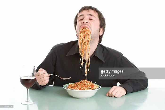 A man in a black shirt greedily eating spaghetti in ecstasy